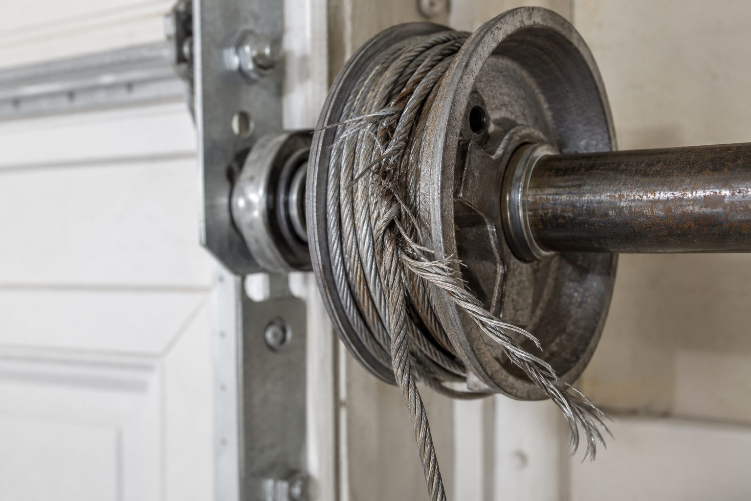 Frayed steel lift cable partially unwound from a garage door cable drum